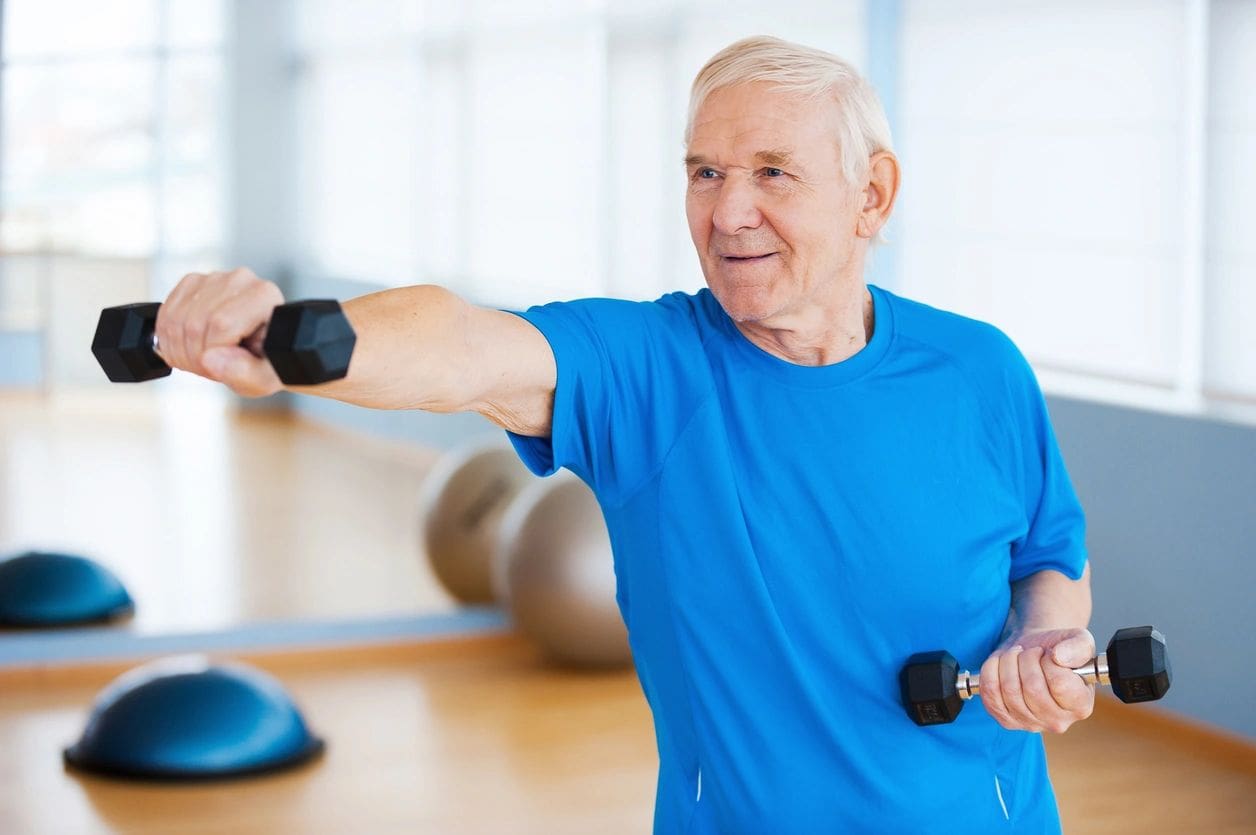 A man is holding two black dumbbells in his hands.